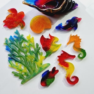 May include: A set of colourful resin sea life figurines, including a seahorse, a turtle, a fish, a seashell, and coral. The figurines are all made in a rainbow colour scheme.