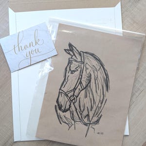May include: A sketch of a horse's head in profile, rendered in black pencil on brown paper. The horse wears a bridle. A small card with "thank you" in gold script is included, along with a white envelope and a clear plastic sleeve.