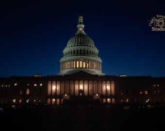 May include: Nighttime photograph of the United States Capitol Building in Washington, D.C. The building is illuminated against a dark blue sky. The dome and columns are lit, and the image includes the text "Jiggy Snapshot Studios".