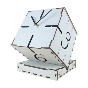 Könnte beinhalten: Eine weiße Holzuhr mit schwarzen Zeigern und Zahlen. Die Uhr ist würfelförmig und auf die Seite gekippt. Die Uhr steht auf einem weißen Holzsockel.