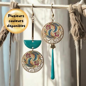 Peut inclure: Une paire de boucles d'oreilles dorées avec un motif bleu sarcelle et blanc. Les boucles d'oreilles présentent un pendentif rond avec un motif floral et un pendentif goutte bleu sarcelle.
