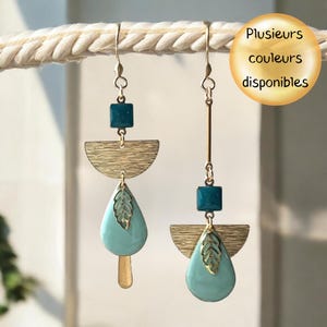 Peut inclure: Une paire de boucles d'oreilles pendantes asymétriques composées d'éléments en métal doré, de perles carrées bleu sarcelle et de breloques en forme de goutte bleu clair avec une feuille dorée. Le visuel inclut le texte "Plusieurs couleurs disponibles".