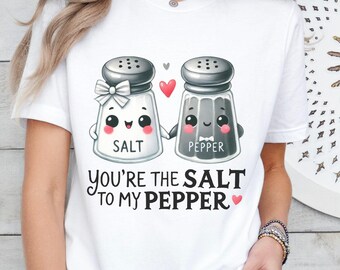 Könnte beinhalten: Weißes T-Shirt mit einem Aufdruck von zwei Salz- und Pfefferstreuern, die sich an den Händen halten. Unter den Streuern steht der Text "You're the salt to my pepper".