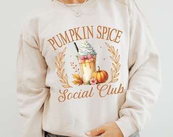May include: A beige sweatshirt with the text "Pumpkin Spice Social Club" in brown lettering. A graphic of a pumpkin spice latte with a pumpkin and fall leaves is centered on the sweatshirt.