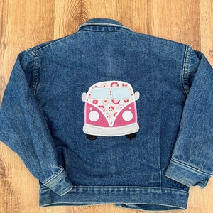 Può includere: Una giacca di jeans blu con una toppa ricamata rosa e bianca di un furgone vintage con fiori sul retro.