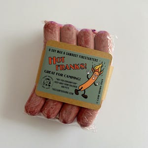 May include: A package of eight soy wax and sawdust firestarters, labeled "Hot Franks!" with a cartoon hot dog illustration. The label reads "Great for Camping!" and "TheCampBrown.com".