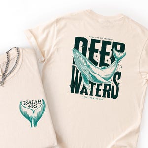 May include: An ivory t-shirt featuring a teal whale tail graphic with the text "ISAIAH 43:2" on the front, and a larger graphic on the back showing a whale with the text "WHEN YOU GO THROUGH DEEP WATERS I WILL BE WITH YOU".