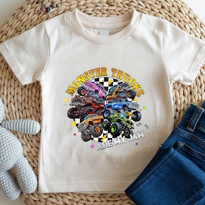 A white t-shirt with a graphic of monster trucks and the text "MONSTER TRUCKS AREMY JAM" printed on it, along with a pair of blue jeans and a crocheted stuffed rabbit.