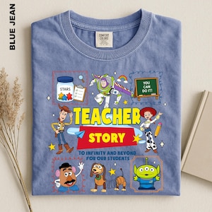A blue t-shirt with a colorful graphic design featuring characters from the Toy Story movie, including Woody, Buzz Lightyear, and other beloved characters. The design also includes a message that says "Teacher Story" and a quote that says "You can do it!"