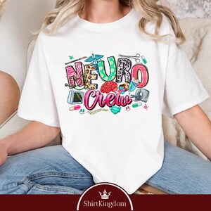 A person wearing a white t-shirt with a colorful graphic design featuring the word "Neuro Crew" and various medical and healthcare-related icons.