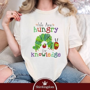 May include: A white t-shirt with a green caterpillar graphic and the text "We Are Hungry for Knowledge".