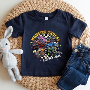 A navy blue t-shirt with a graphic of monster trucks and the text "MONSTER TRUCKS ARE MY JAM" printed on it, along with a pair of blue jeans and a crocheted rabbit toy.