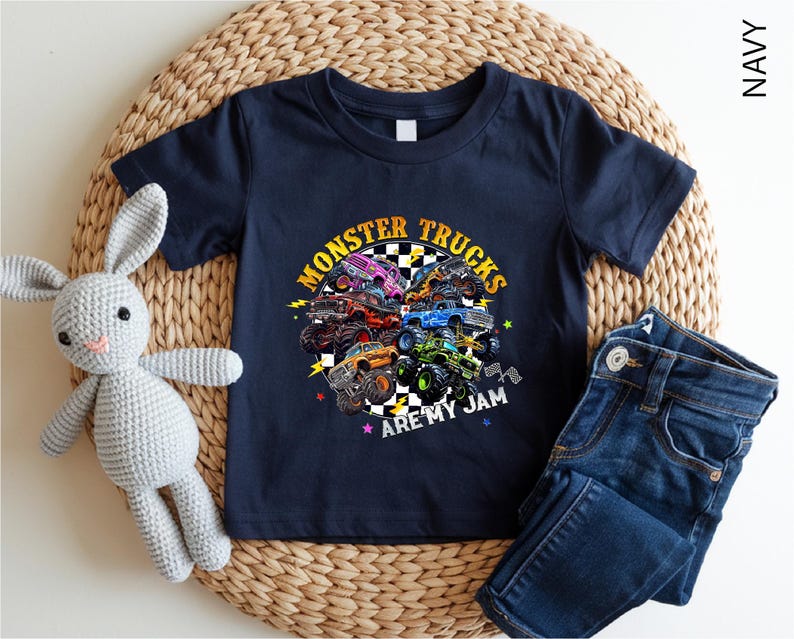A navy blue t-shirt with a graphic of monster trucks and the text "MONSTER TRUCKS ARE MY JAM" printed on it, along with a pair of blue jeans and a crocheted rabbit toy.