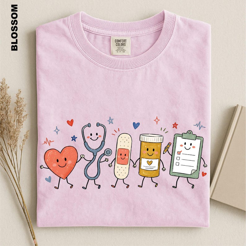 A pink t-shirt with a cartoon illustration of a stethoscope, heart, bandage, pill bottle, clipboard, and other medical-themed characters.