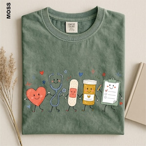 a green t-shirt with a playful design of cartoon-style medical professionals, including a stethoscope, heart, bandage, pill bottle, clipboard, and a smiling face.