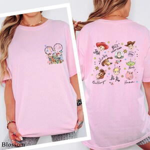 A woman wearing a pink t-shirt with various cartoon characters and text printed on it.