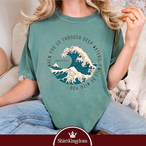 May include: A light green t-shirt with a graphic of a blue wave and the text "WHEN YOU GO THROUGH DEEP WATERS. I WILL BE WITH YOU" and "ISAIAH 43:2".