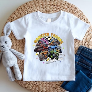 A white t-shirt with a graphic of monster trucks and the text "MONSTER TRUCKS ARE MY JAM" printed on it, along with a crocheted rabbit toy and a pair of blue jeans.