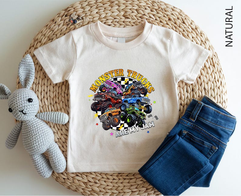 A white t-shirt with a graphic of monster trucks and the text "MONSTER TRUCKS AREMY JAM" printed on it, along with a pair of blue jeans and a crocheted stuffed rabbit.