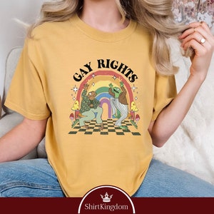 May include: A mustard yellow t-shirt with a rainbow, two frogs dancing, and the text "Gay Rights".