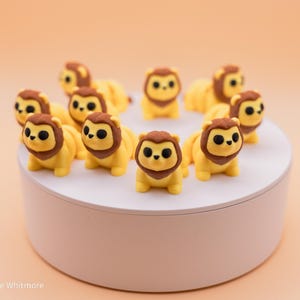 May include: A circle of ten small, yellow lion figurines with brown manes and black eyes. The figurines are arranged in a circle on a white circular platform.