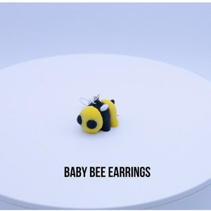 May include: A pair of yellow and black bee earrings with white accents. The earrings are made of polymer clay and have silver hooks.