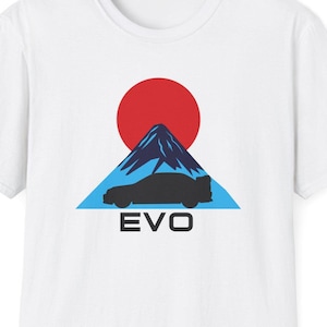 Może przedstawiać: Biała koszulka z grafiką czarnego samochodu przed niebiesko-białą górą z czerwonym słońcem z tyłu. Tekst "EVO" jest nadrukowany pod samochodem.