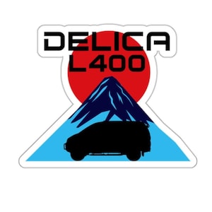 May include: A sticker featuring a black silhouette of a Mitsubishi Delica L400 van driving up a blue and white mountain with a red sun behind it. The text "DELICA L400" is above the mountain.