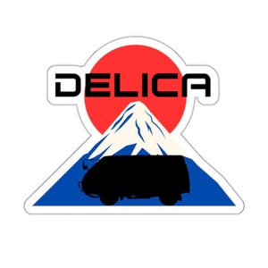 Op de afbeelding: Een sticker met een silhouet van een bestelwagen die de berg Fuji op rijdt, met een rode zon en het woord "DELICA" in zwarte tekst.
