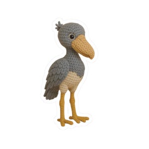May include: A handcrafted crochet Shoebill Stork figure. The bird features a grey body, a tan beak, and yellow legs and feet. This Shoebill Stork is a unique and whimsical decorative item.