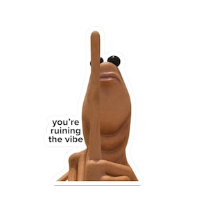 Puede incluir: Una pegatina con una figura de dibujos animados con cuerpo marrón, ojos negros y el dedo corazón levantado. El texto "you're ruining the vibe" está impreso en negro sobre fondo blanco.