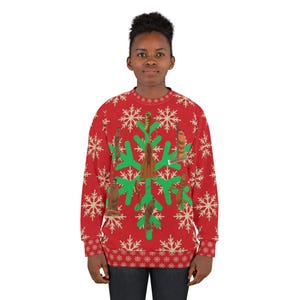 May include: Red Christmas sweater featuring a snowflake pattern and a green snowflake design in the centre. The green snowflake design has brown figures on it. The sweater has a crew neck and long sleeves.
