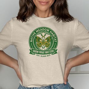 Cream t-shirt with green circular logo "Native Meadow Habitat Grow What Matters Est. 10,000 BCE".