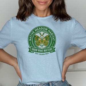 Pale blue t-shirt with green and yellow "Native Meadow Habitat" circular logo.