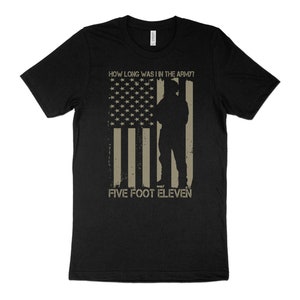 May include: Black t-shirt featuring a distressed American flag design with a soldier silhouette. The text reads "HOW LONG WAS I IN THE ARMY?" above and "FIVE FOOT ELEVEN" below the flag graphic.