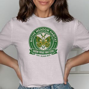 White t-shirt with a circular Native Meadow Habitat logo featuring butterflies and text.
