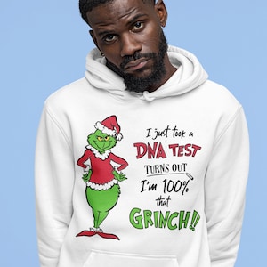 Puede incluir: Sudadera con capucha blanca con un personaje verde del Grinch que lleva un gorro de Papá Noel. El texto en la sudadera dice "Acabo de hacerme una prueba de ADN, resulta que soy 100% ese Grinch!"