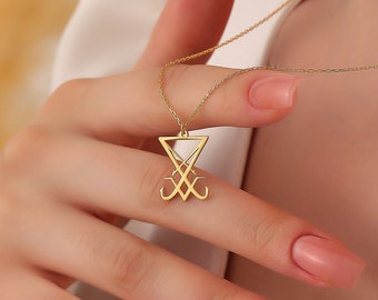 May include: A gold necklace with a pendant featuring a stylized symbol in a triangle. The symbol is a combination of lines and curves.