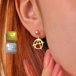 May include: Gold earring with an anarchy symbol pendant. The earring is made of 14k solid gold.