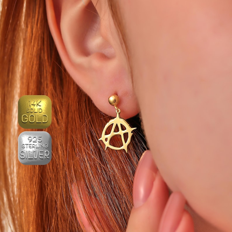 May include: Gold earring with an anarchy symbol pendant. The earring is made of 14k solid gold.