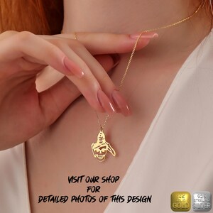 K&ouml;nnte beinhalten: Eine goldene Halskette mit einem Anh&auml;nger, der einen Sch&auml;del mit Hut zeigt. Der Anh&auml;nger ist aus massivem Gold und die Kette aus Sterlingsilber. Die Halskette wird von einer Person getragen, deren Hand die Kette h&auml;lt.