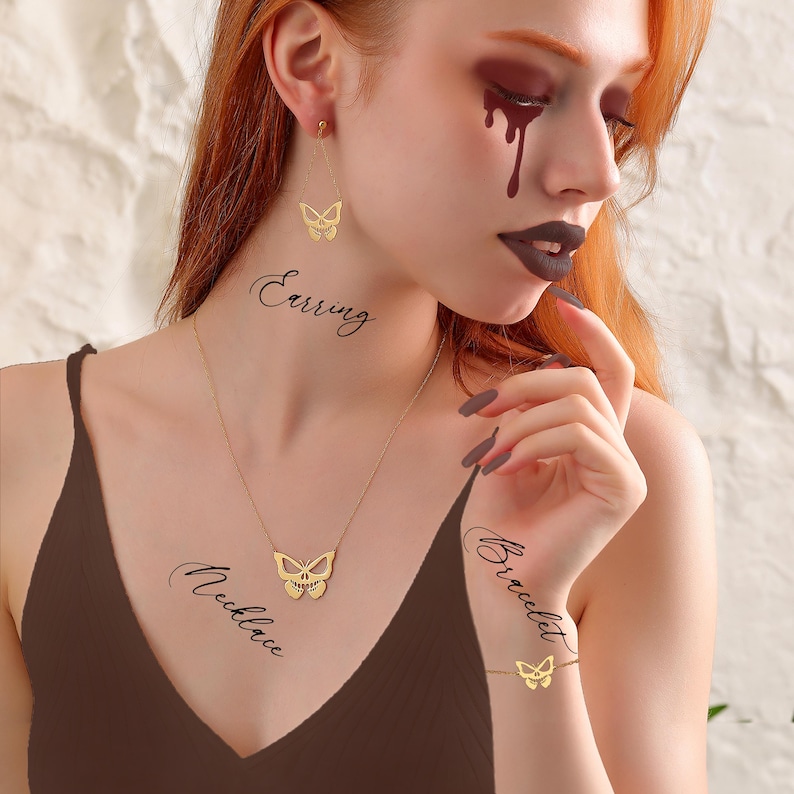 K&ouml;nnte beinhalten: Eine goldene Schmetterlingskette, ein Armband und Ohrringe. Der Schmuck wird von einem Model mit dunkelrotem Augen-Make-up und einem braunen Oberteil getragen.