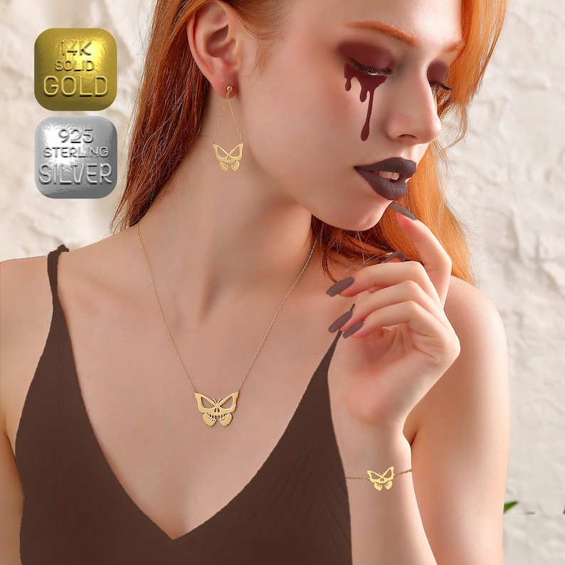 May include: A woman wearing a brown top with a gold butterfly necklace and matching earrings. She is also wearing a gold butterfly bracelet on her wrist. The necklace and earrings are available in 14k solid gold or 925 sterling silver.