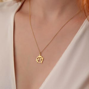 May include: A gold chain necklace with a pendant in the shape of an anarchy symbol.