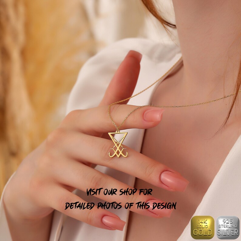 May include: A gold necklace with a pendant featuring the sigil of Baphomet, a triangular symbol with two intertwined heads. The necklace is worn by a person with their hand holding the pendant. The image includes the text "VISIT OUR SHOP FOR DETAILED PHOTOS OF THIS DESIGN" and two labels: "14K SOLID GOLD" and "925 STERLING SILVER".