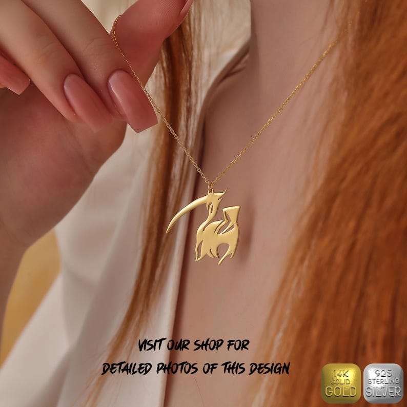 May include: A gold necklace with a stylized animal pendant. The pendant is a silhouette of a goat with its head turned to the side. The necklace is on a model's neck. The text "VISIT OUR SHOP FOR DETAILED PHOTOS OF THIS DESIGN" is below the image. There are two small squares below the text, one with the text "14K SOLID GOLD" and the other with the text "925 STERLING SILVER".