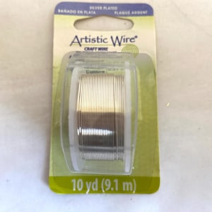 May include: A spool of silver-plated Artistic Wire craft wire, 10 yards (9.1 meters) long. The wire is wound around a clear plastic spool and packaged in a green and white cardboard box.