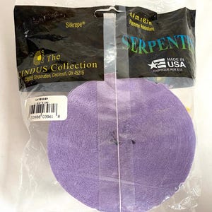 May include: A roll of lavender crepe paper ribbon, labeled "Serpentine," is packaged in clear plastic. The packaging includes text such as "Silkrepe" and "The Cindus Collection." The ribbon measures 1.75 inches by 150 feet.