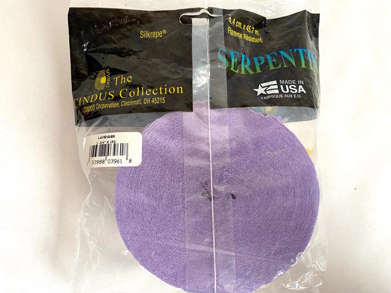 May include: A roll of lavender crepe paper ribbon, labeled "Serpentine," is packaged in clear plastic. The packaging includes text such as "Silkrepe" and "The Cindus Collection." The ribbon measures 1.75 inches by 150 feet.