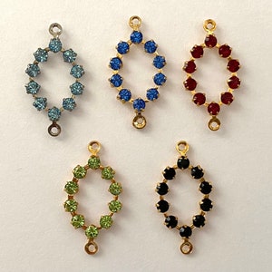 May include: Five oval-shaped metal charms with a gold finish. Each charm has a ring of colorful rhinestones around the perimeter. The charms are blue, red, green, black, and light blue.